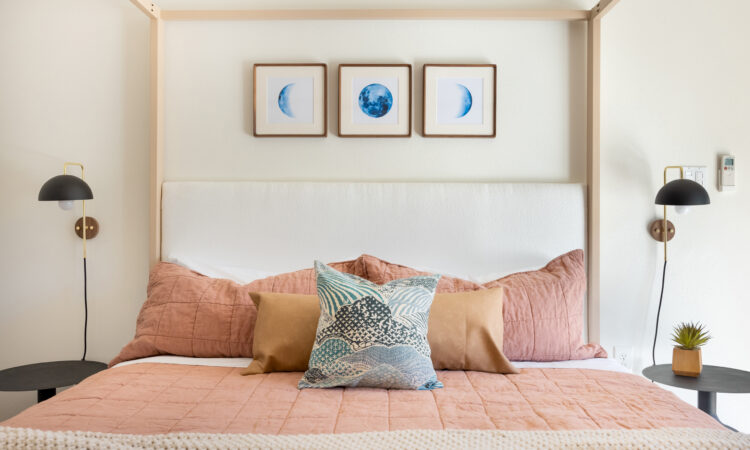 Cozy bedroom with blush bedding, decorative pillows, and modern lighting, featuring framed moon phase artwork above the bed.